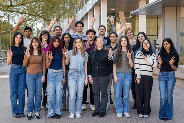 The Verpeut Lab making the pitchfork hand gesture, standing in front of a modern building with glass windows.